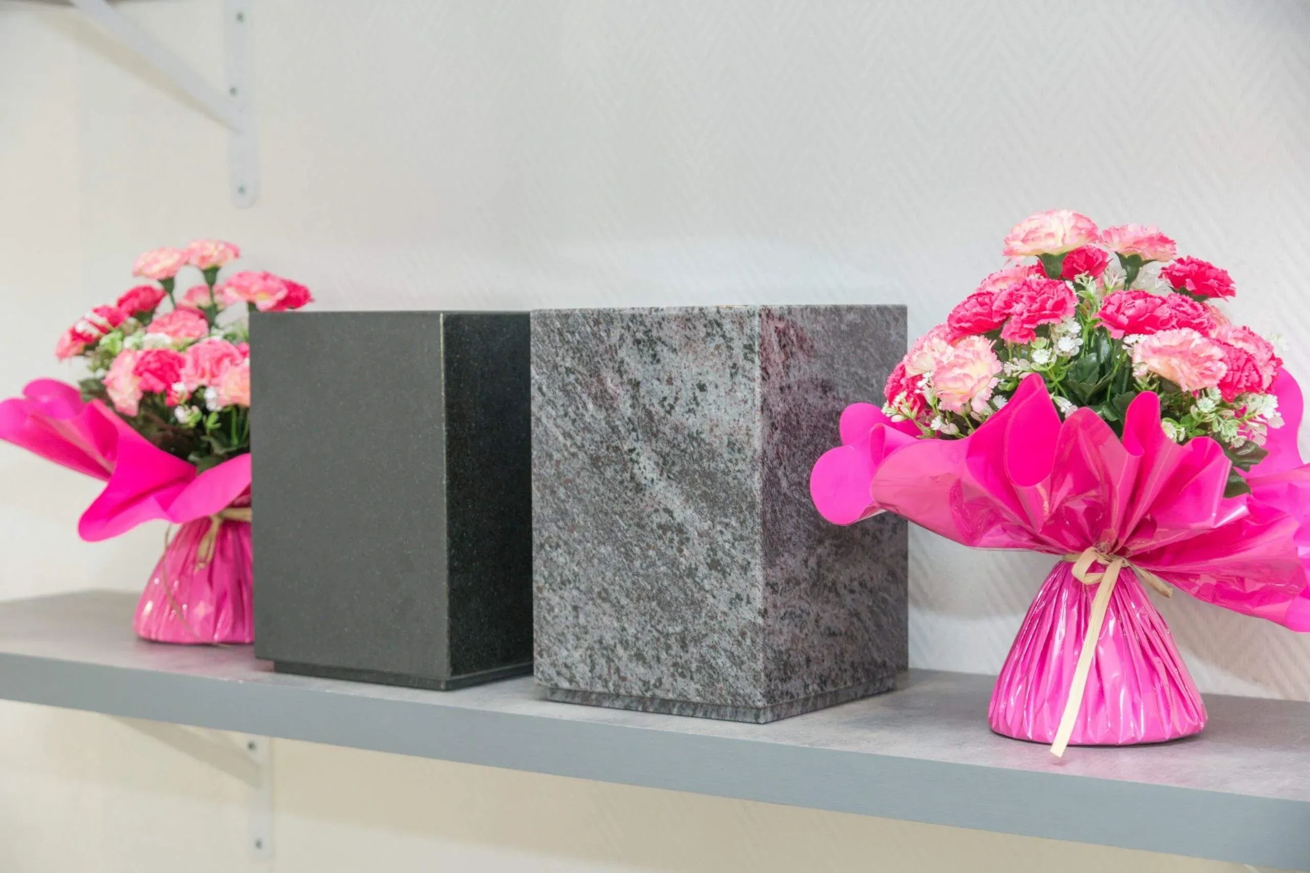 Urnes funéraires en granit exposées sur étagère aux côtés de bouquets de fleurs artificielles