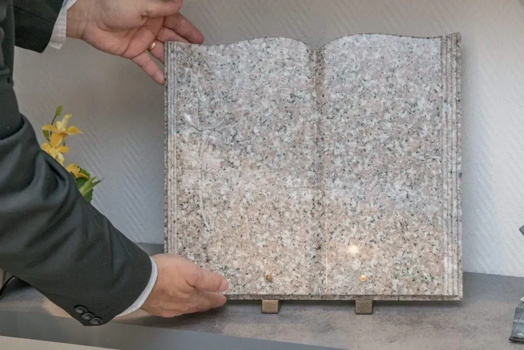 Main présentant une plaque funéraire personnalisable en granit en forme de livre ouvert