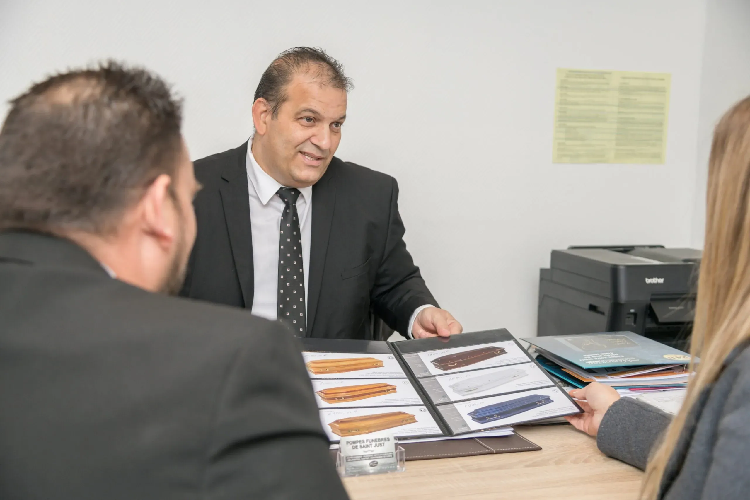 Conseiller funéraire présentant un catalogue de modèles de cercueils lors d'un entretien en bureau
